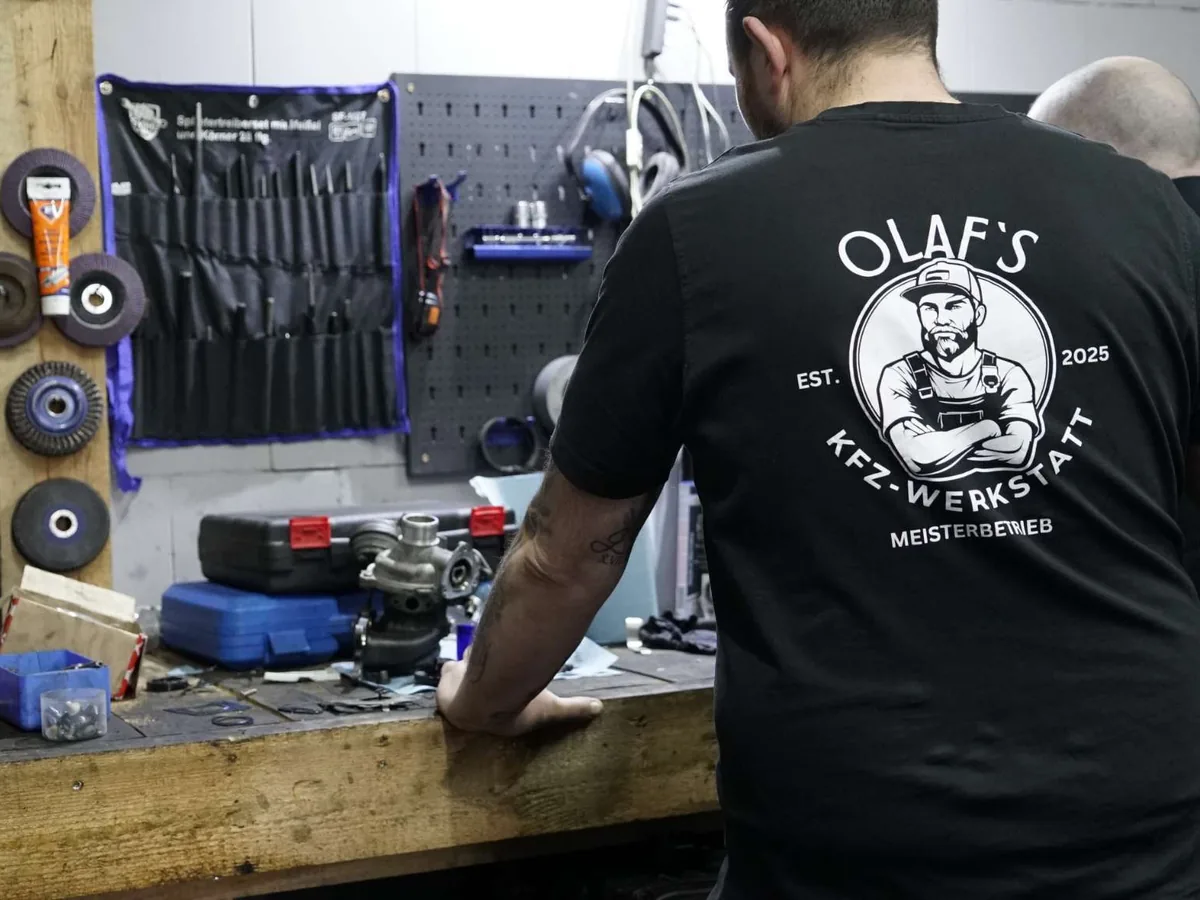 Kollege im Firmen-Shirt von Olaf's Werkstatt an der Werkbank